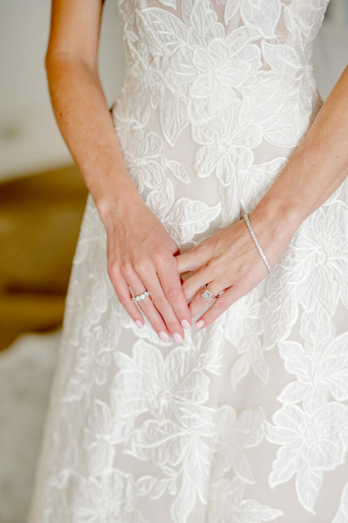 Bride's hands in lace dress display rings, bracelet.