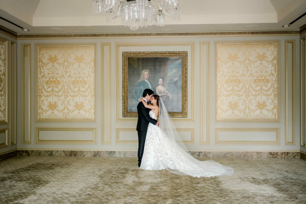 Bride and groom kiss in ornate, gold-accented room.
