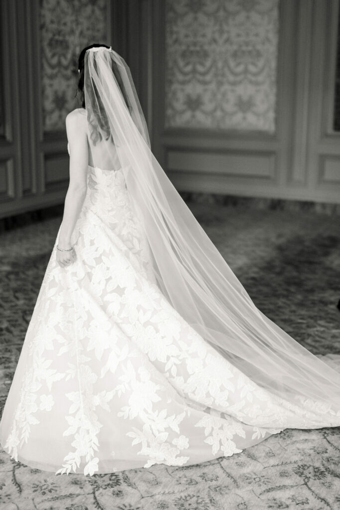 Bride in floral lace gown with long train indoors.
