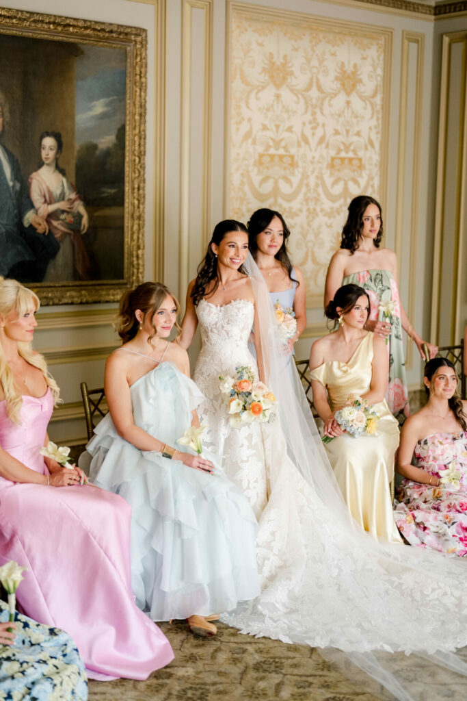 Bride and six bridesmaids in luxury gowns indoors.