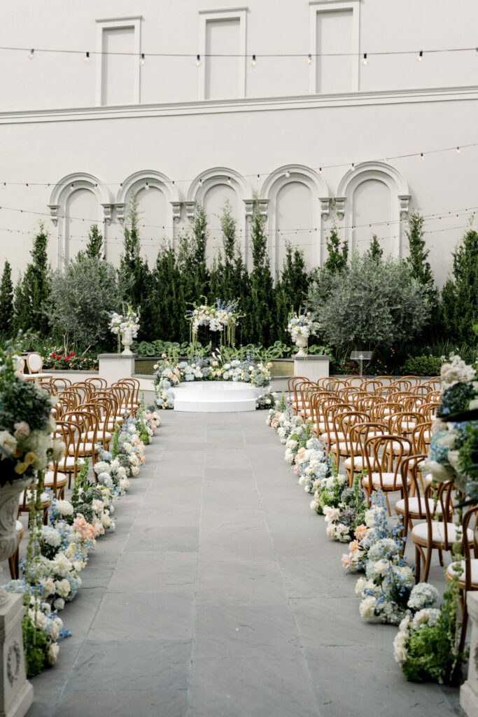 Elegant wedding aisle, floral arch, wood chairs, greenery.