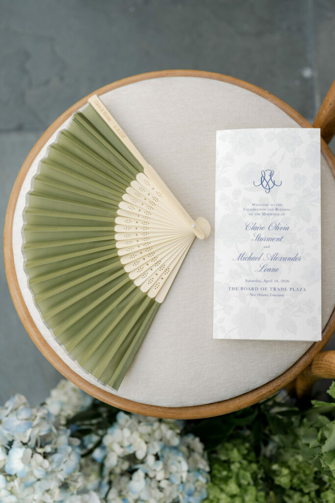 Green fan, wedding program, flowers on cushioned chair.