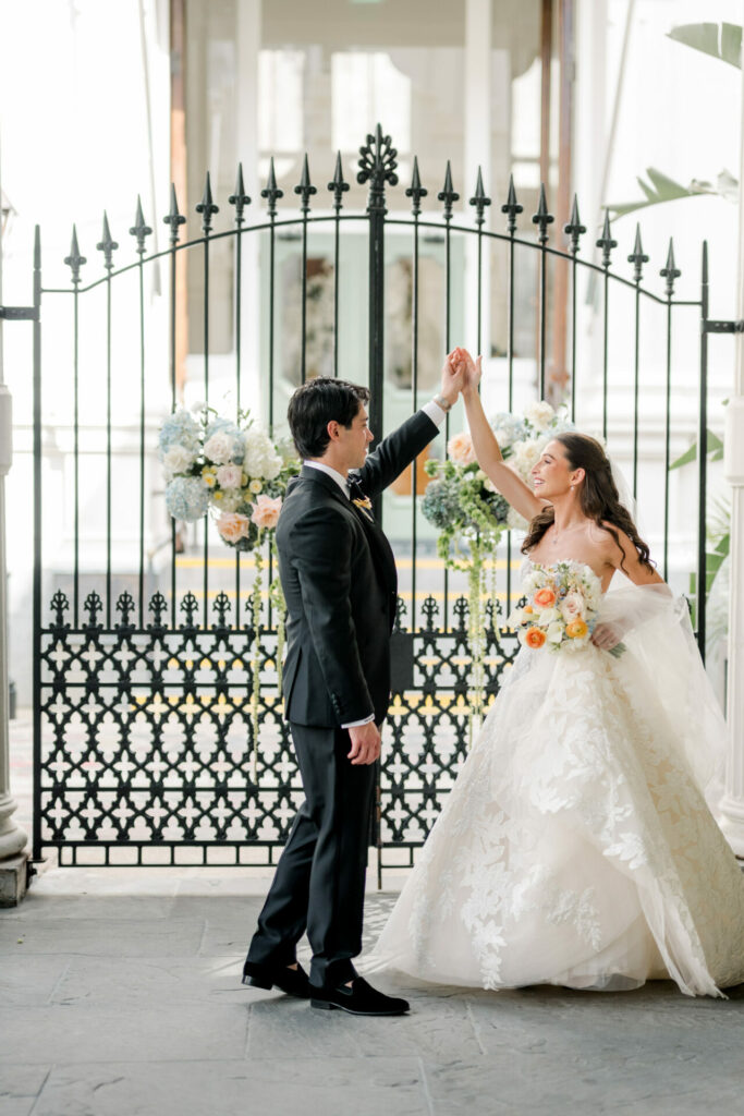 Bride and groom dance, smiling by floral iron gate.