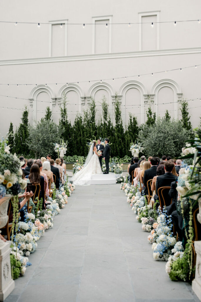 Bride and groom at lush outdoor altar under string lights.
