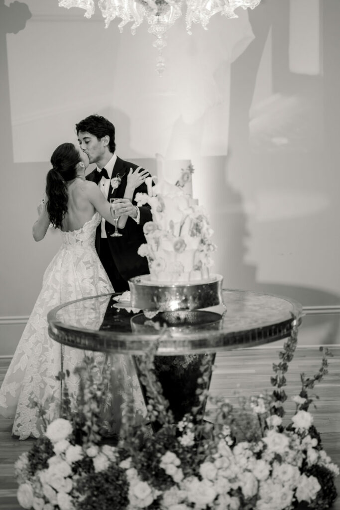 Bride and groom kiss with champagne, luxe cake, florals.