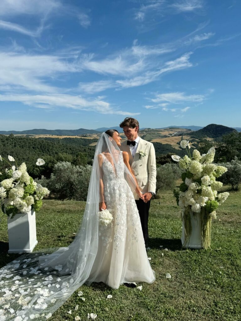Smiling newlyweds outdoors with hills and florals.