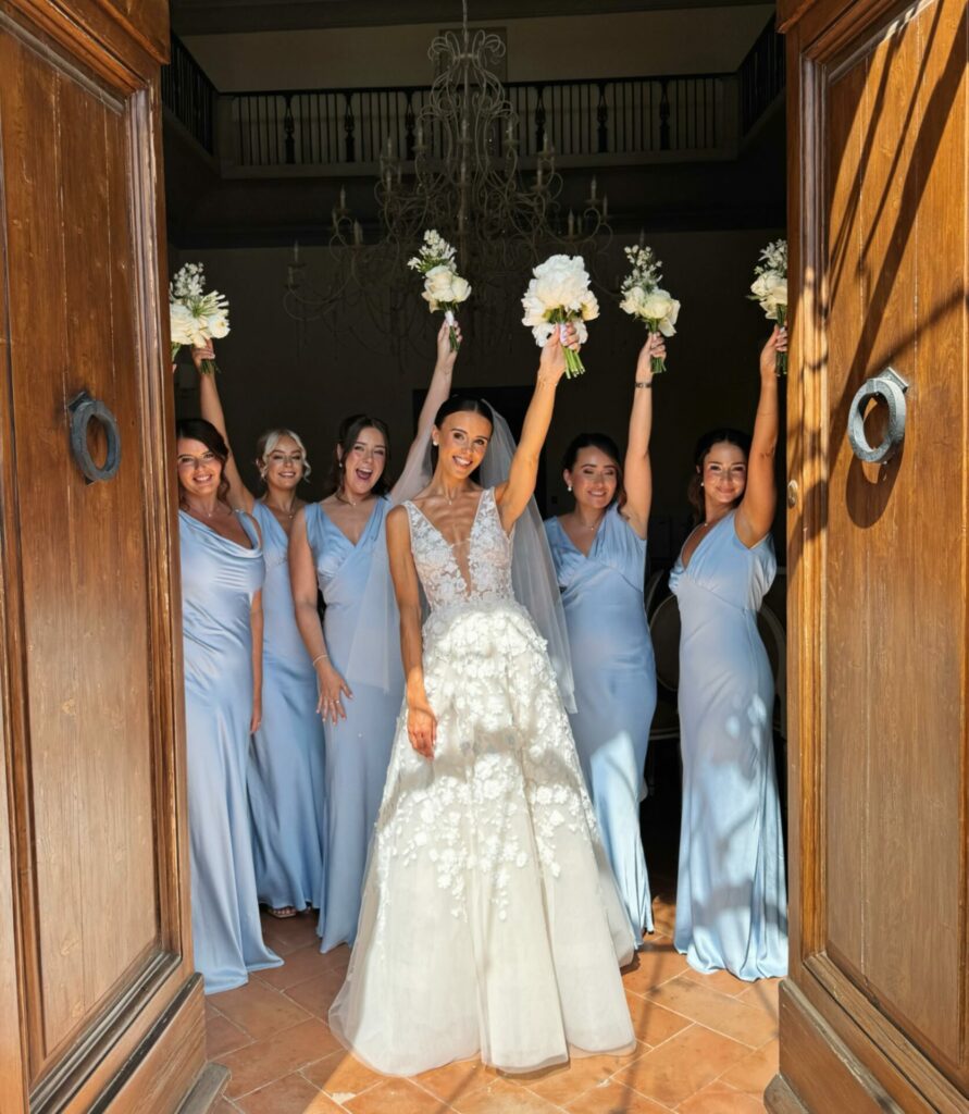 Bride and bridesmaids smiling with bouquets raised.
