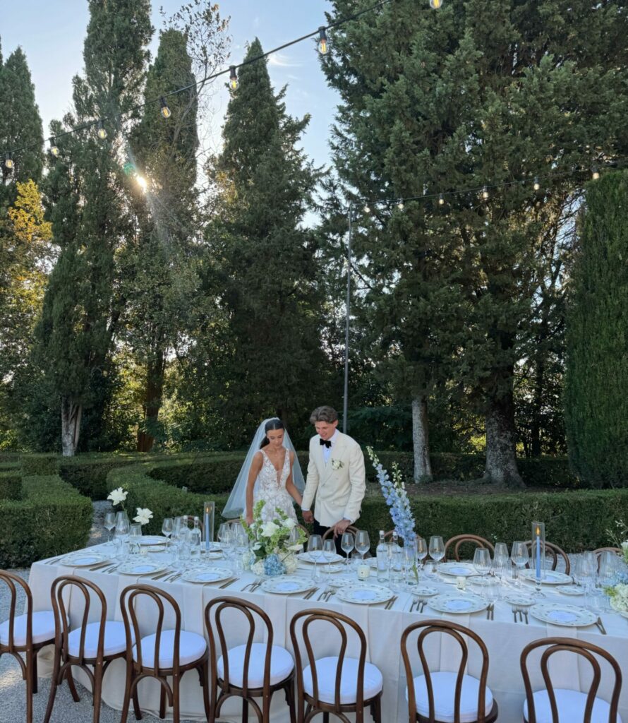 Bride and groom by elegant outdoor table, sunlit garden.
