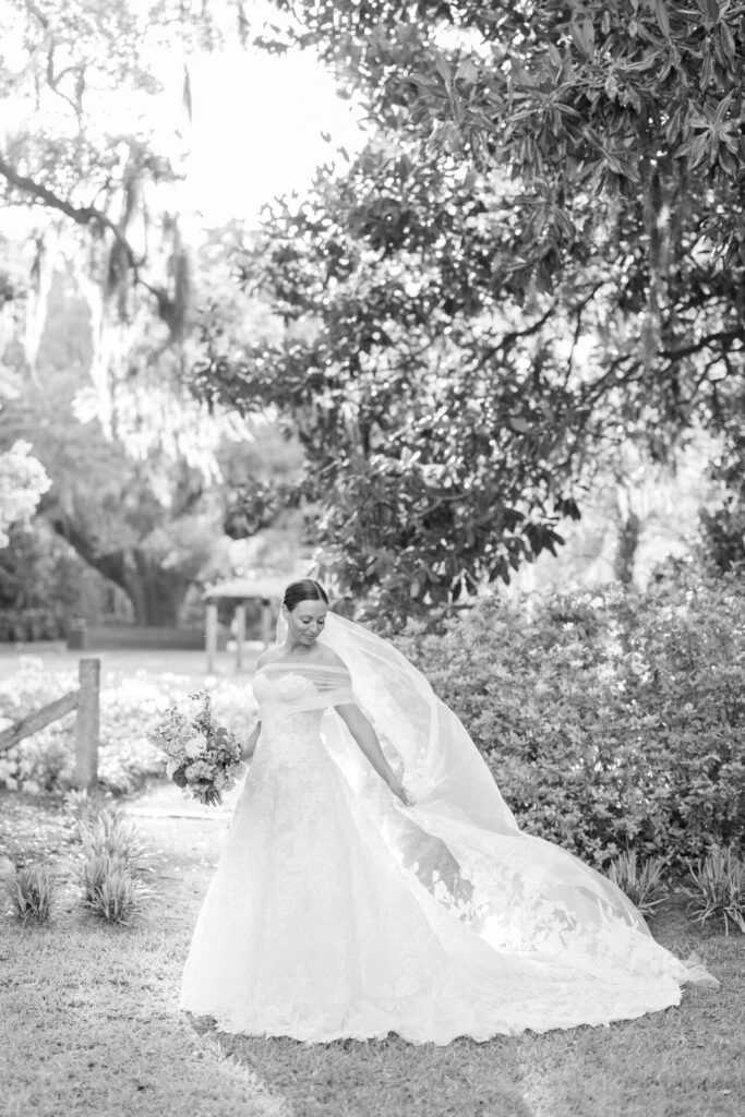 Bride in white gown stands in sunlit garden.