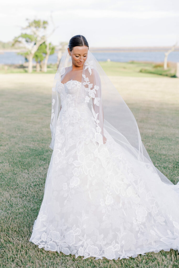 Bride in lace gown and veil, serene outdoors.