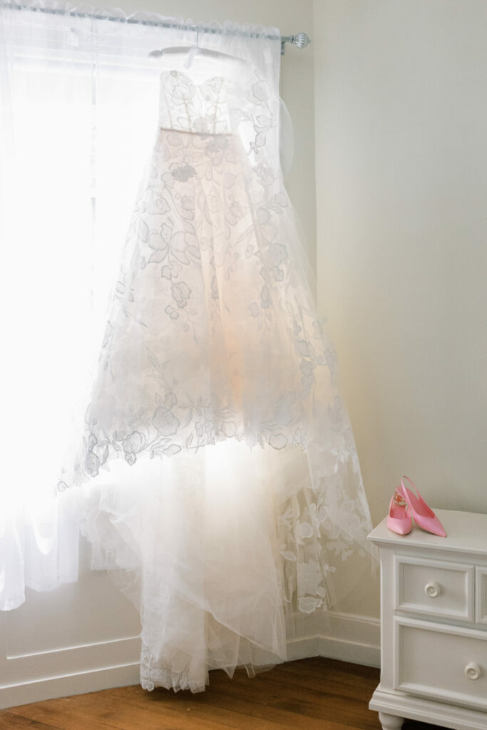 White floral dress by window, pink shoes nearby.