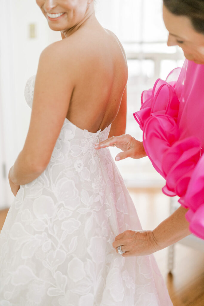 Bride in floral dress helped by woman in pink.