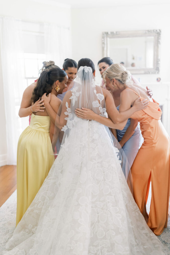 Bride in couture gown hugs pastel-dressed bridesmaids.