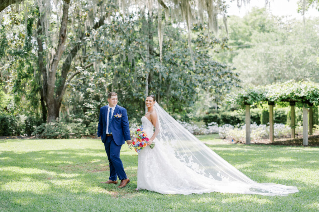 Bride and groom walking on lawn under trees.