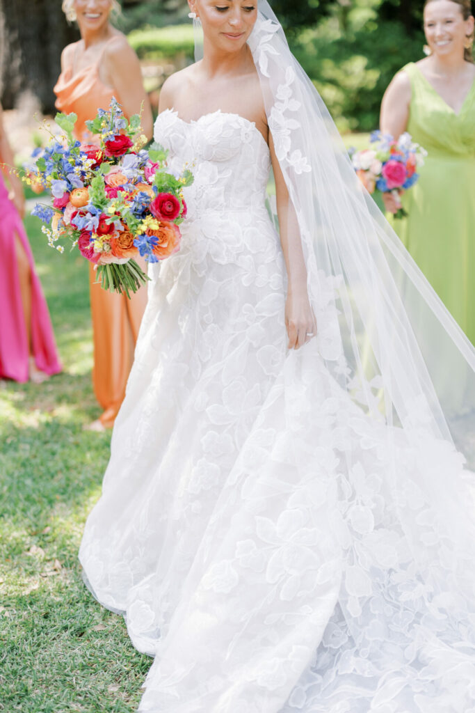 Bride in lace gown with bouquet, bridesmaids behind.