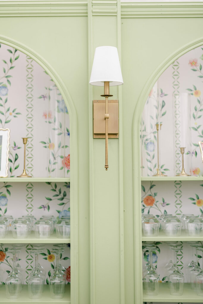 Brass sconce, floral wallpaper, glassware, pastel green wall.