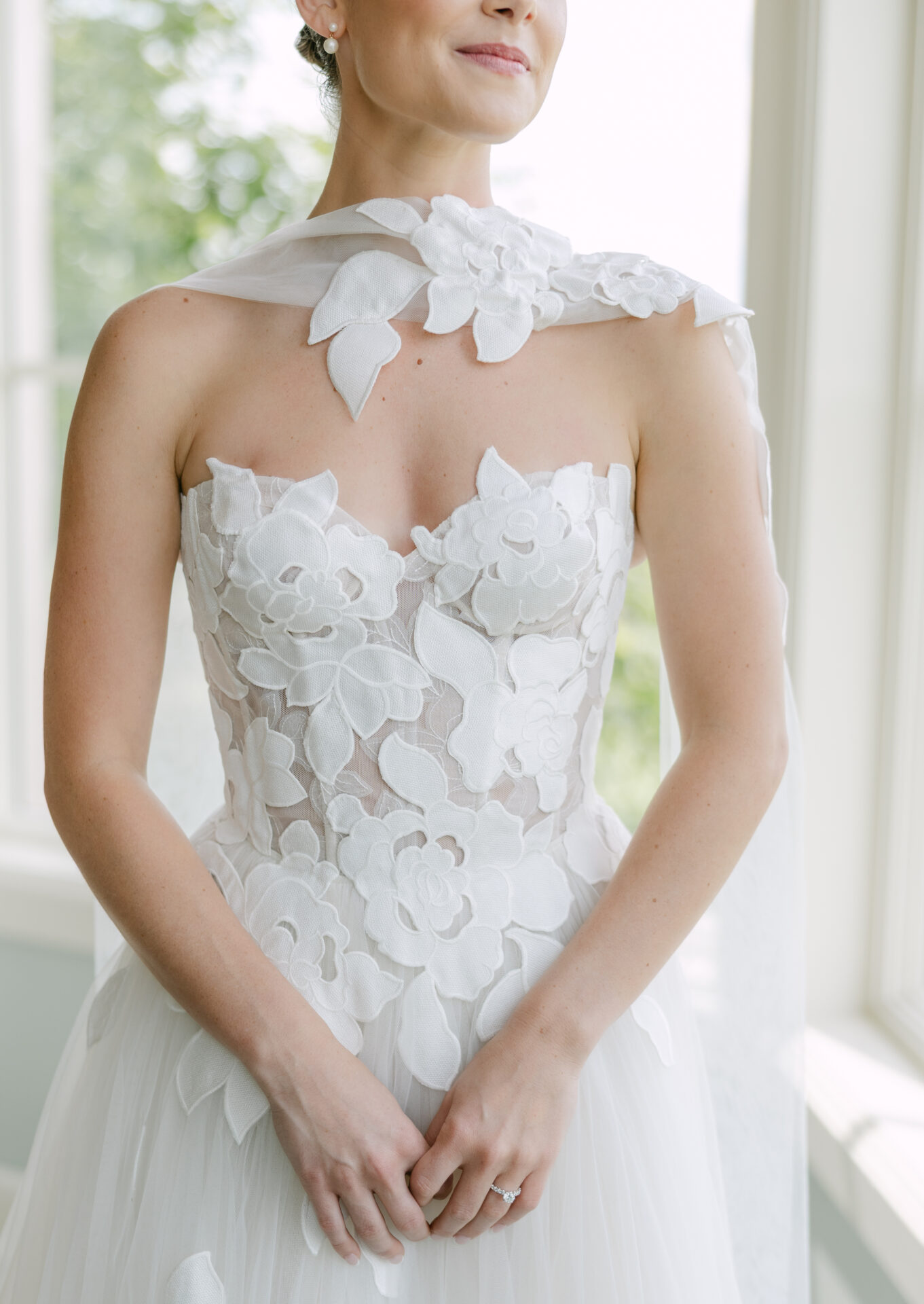 Bride in floral white dress by sunny window.