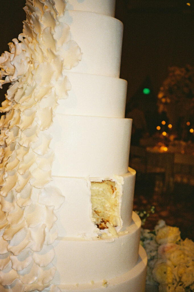 Elegant white wedding cake, slice missing, romantic setting.