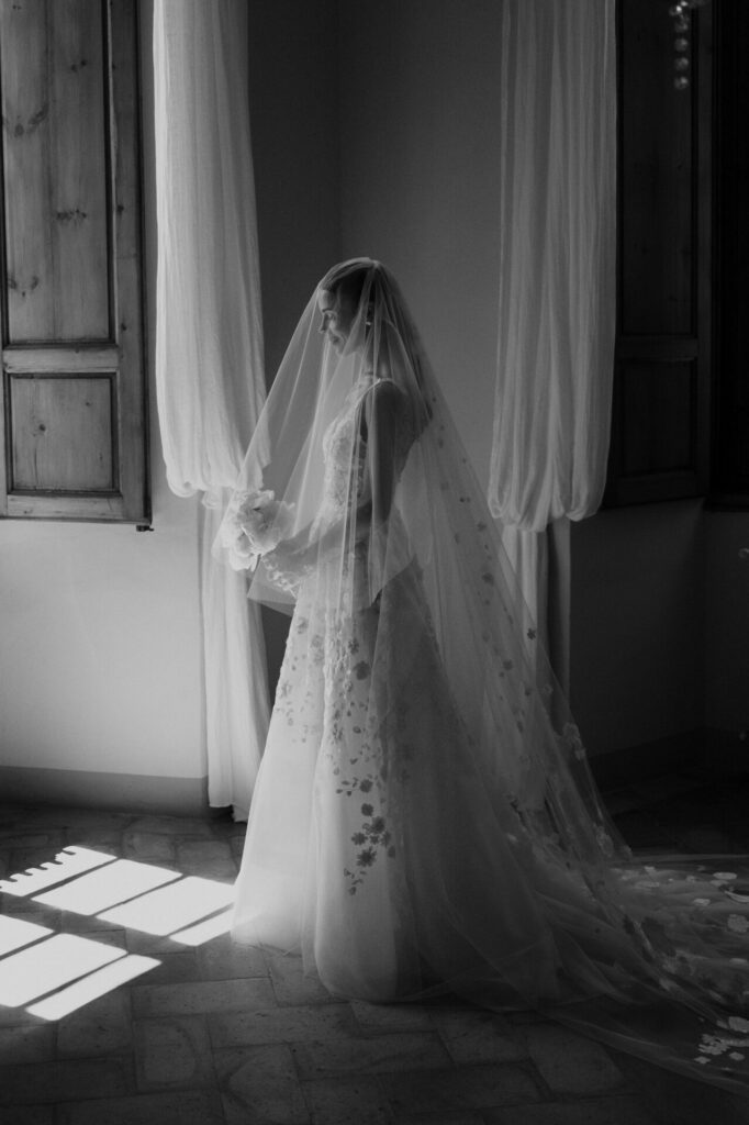 Bride in window light, elegant veil, black and white.
