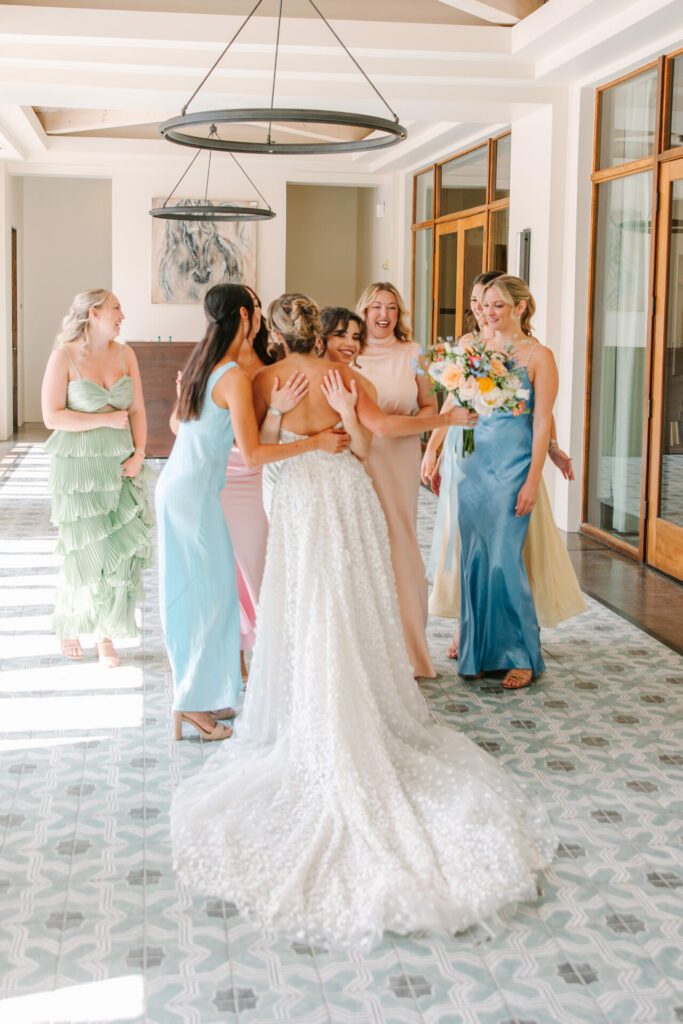 Bride in pearl gown hugs bridesmaids in hallway.