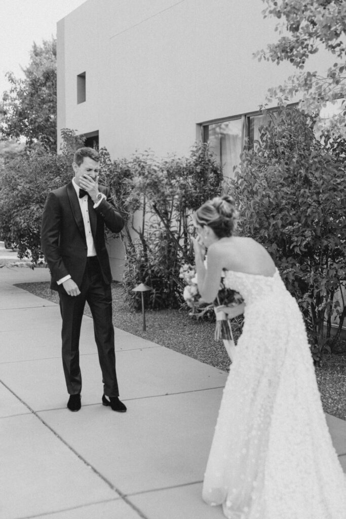 Bride and groom covering faces outdoors, elegant, black-and-white.