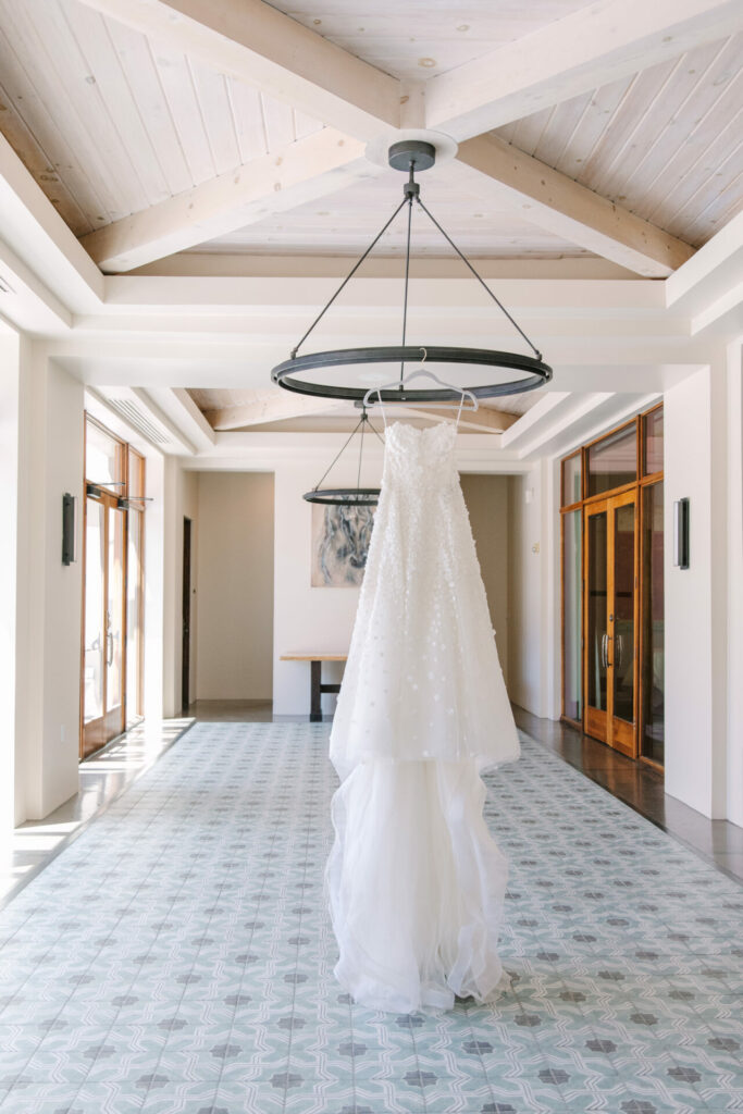 White couture wedding dress hangs in airy room.