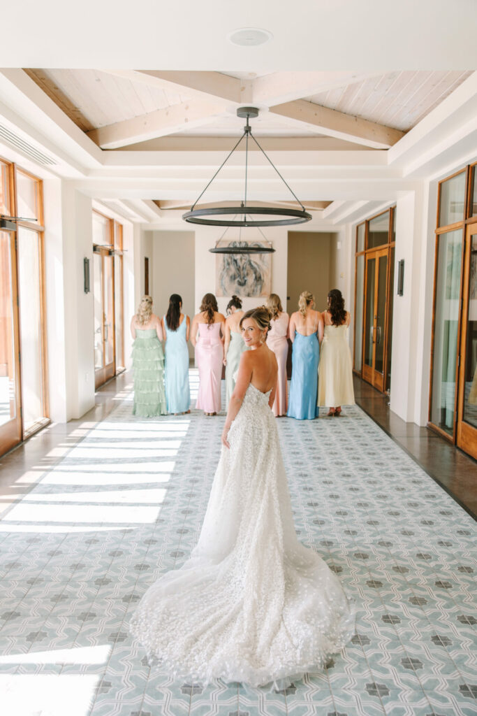 Smiling bride poses, bridesmaids in pastels turned away.