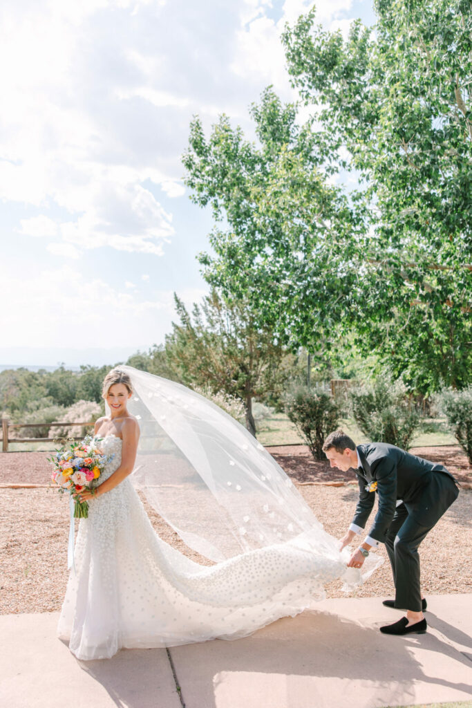 Bride Katya Ruiz smiles as groom adjusts veil outdoors.