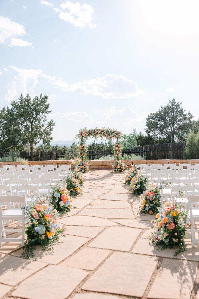 Elegant outdoor wedding aisle, white chairs, floral arch.