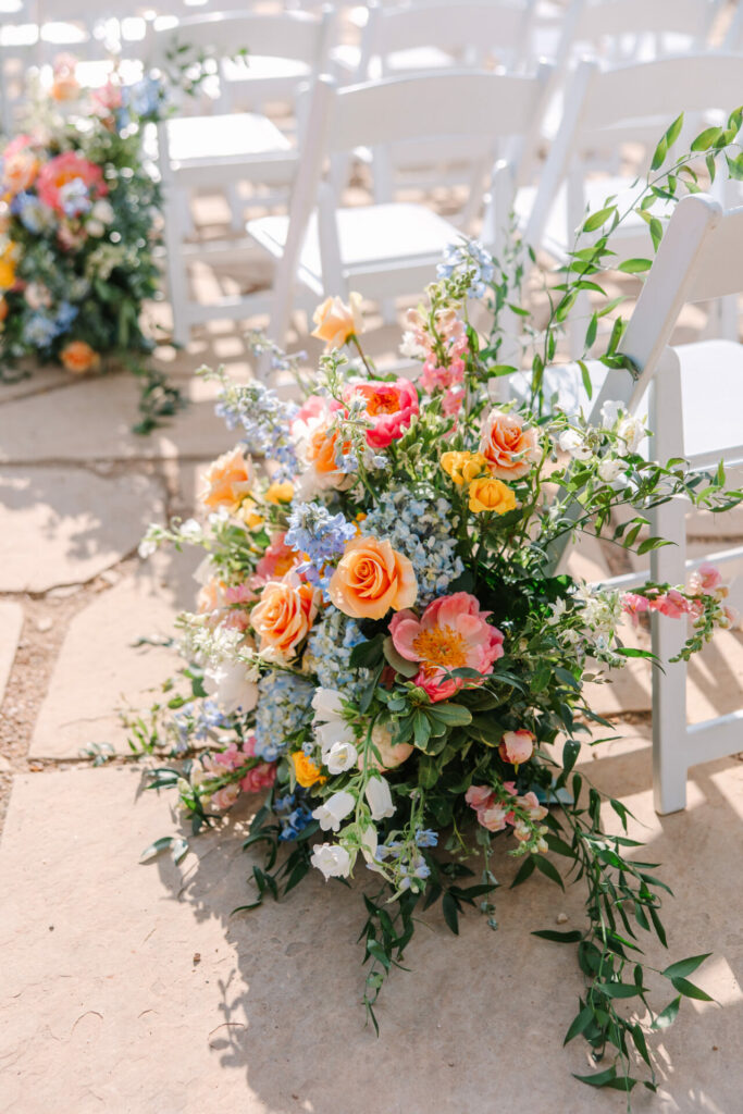 Floral aisle decor with roses, greenery, blue blooms.