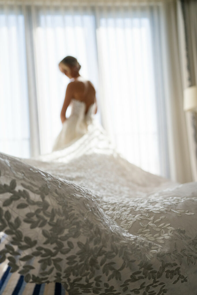 Bride in sunlit window wearing luxury embroidered gown.