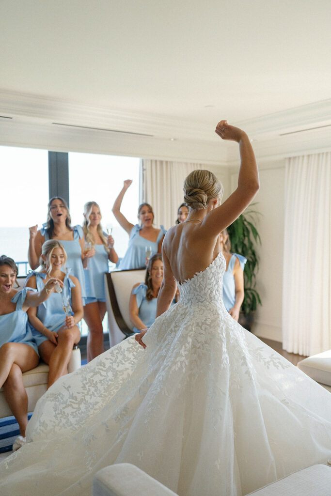 Bride celebrates, bridesmaids cheer in bright room.