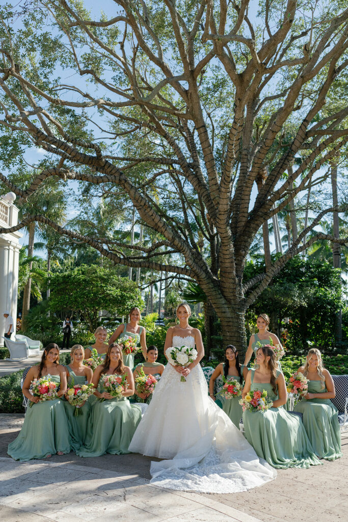 Bride and bridesmaids pose under tree outdoors.