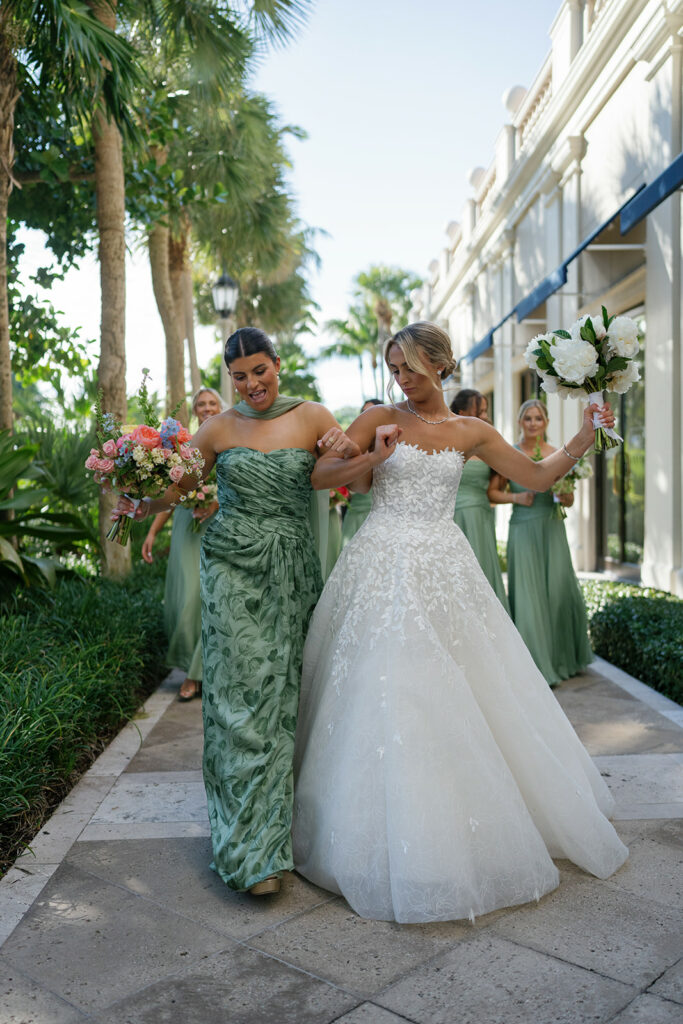 Smiling bride and bridesmaids walk on sunny path.