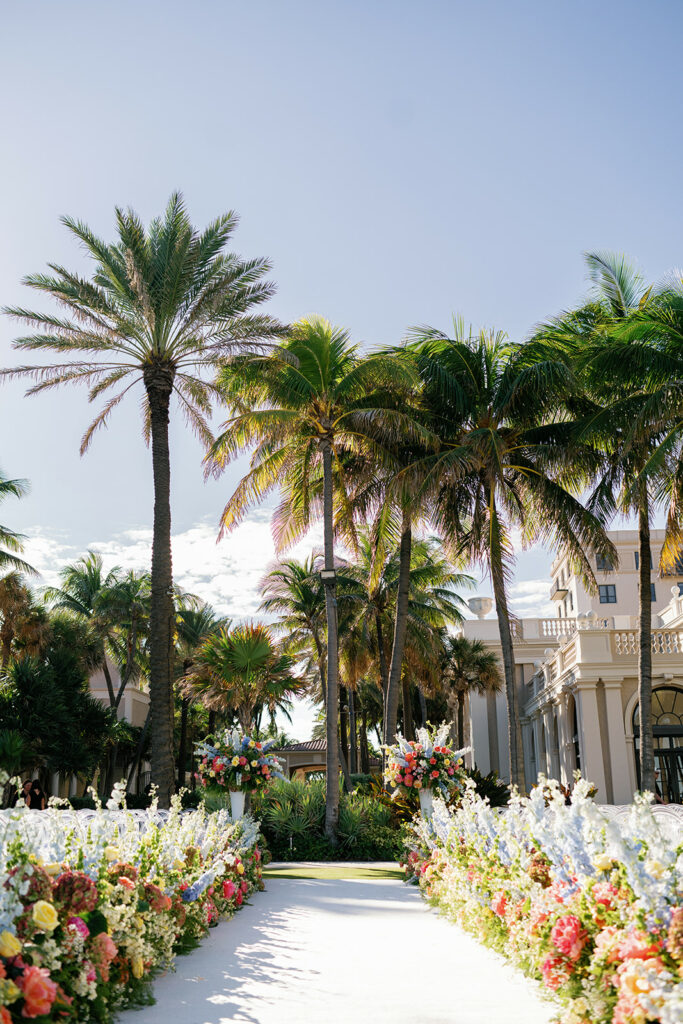 Elegant sunlit aisle, flowers, palms, luxury venue.
