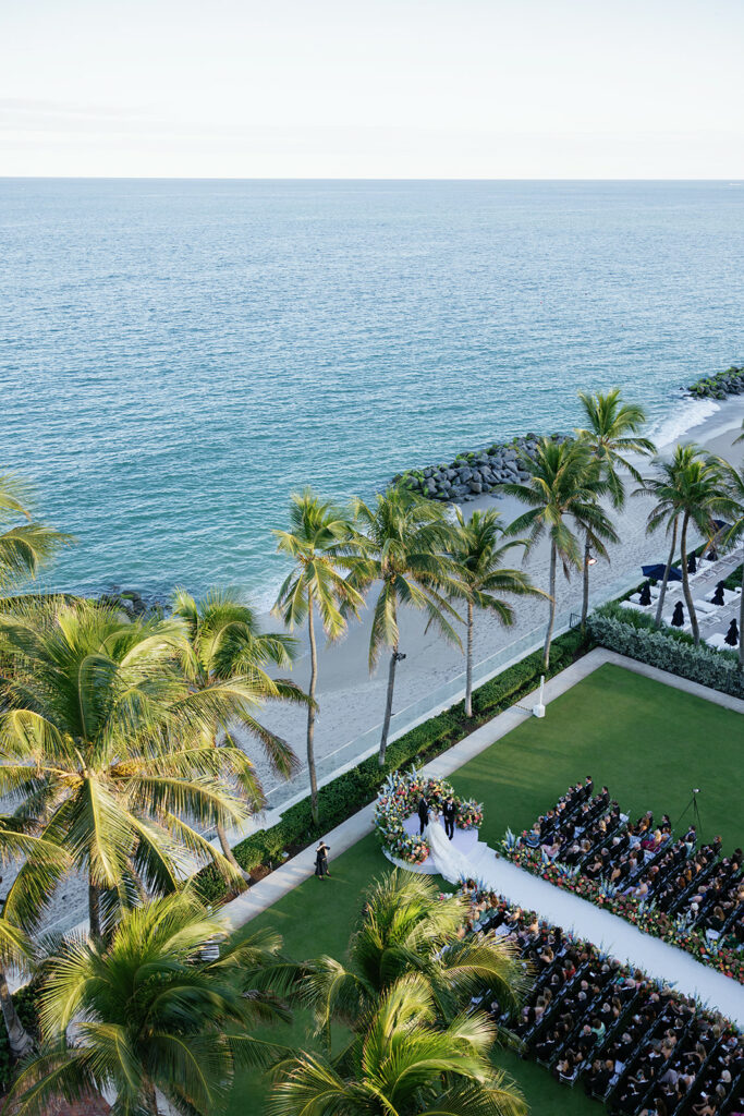 Outdoor wedding on lawn by beach, guests seated.
