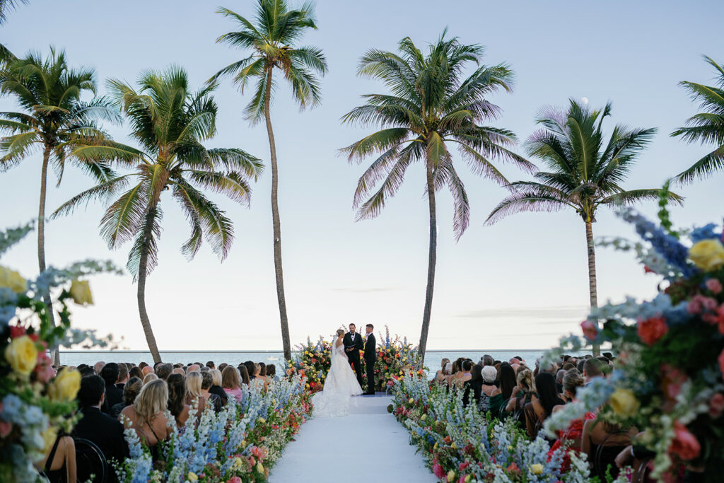 Bride and groom at beach altar with guests.
