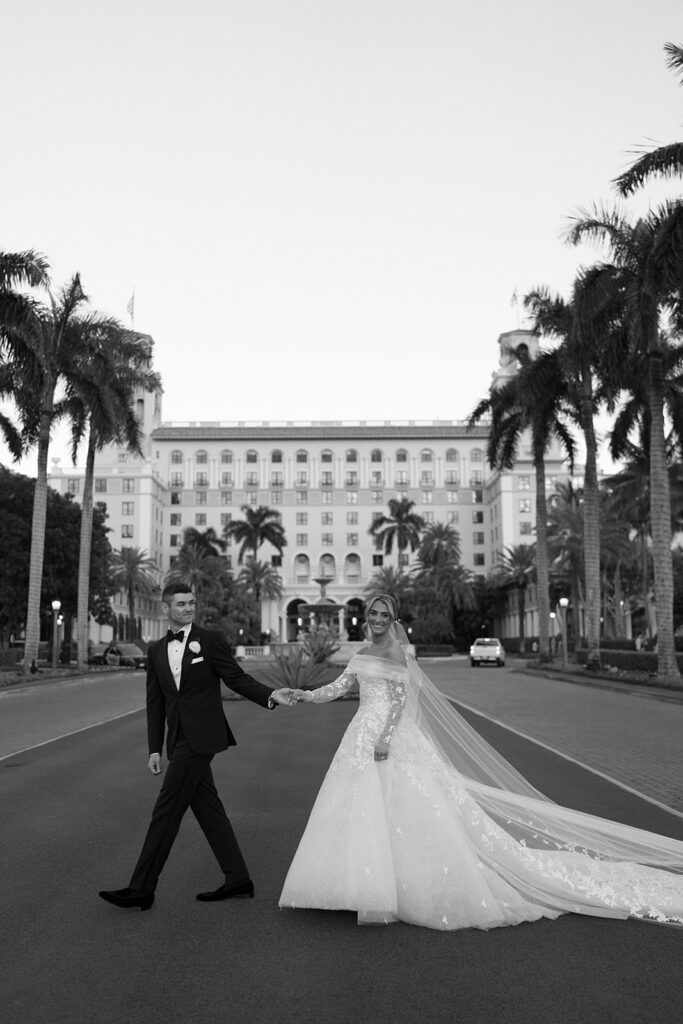 Bride and groom cross street in elegant attire.