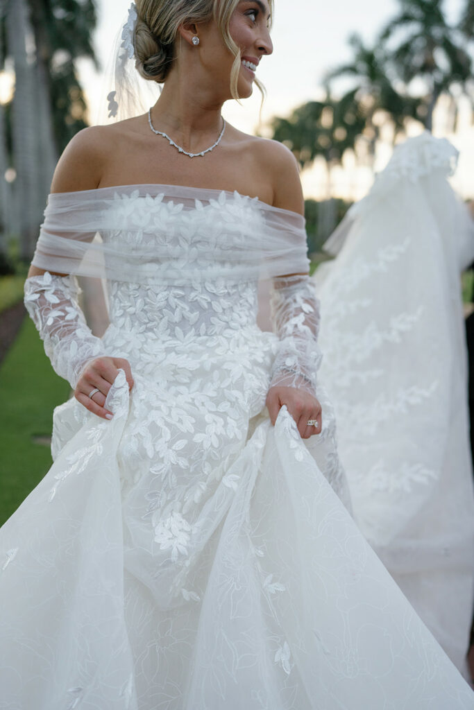 Bride in floral gown smiles outdoors with palms.