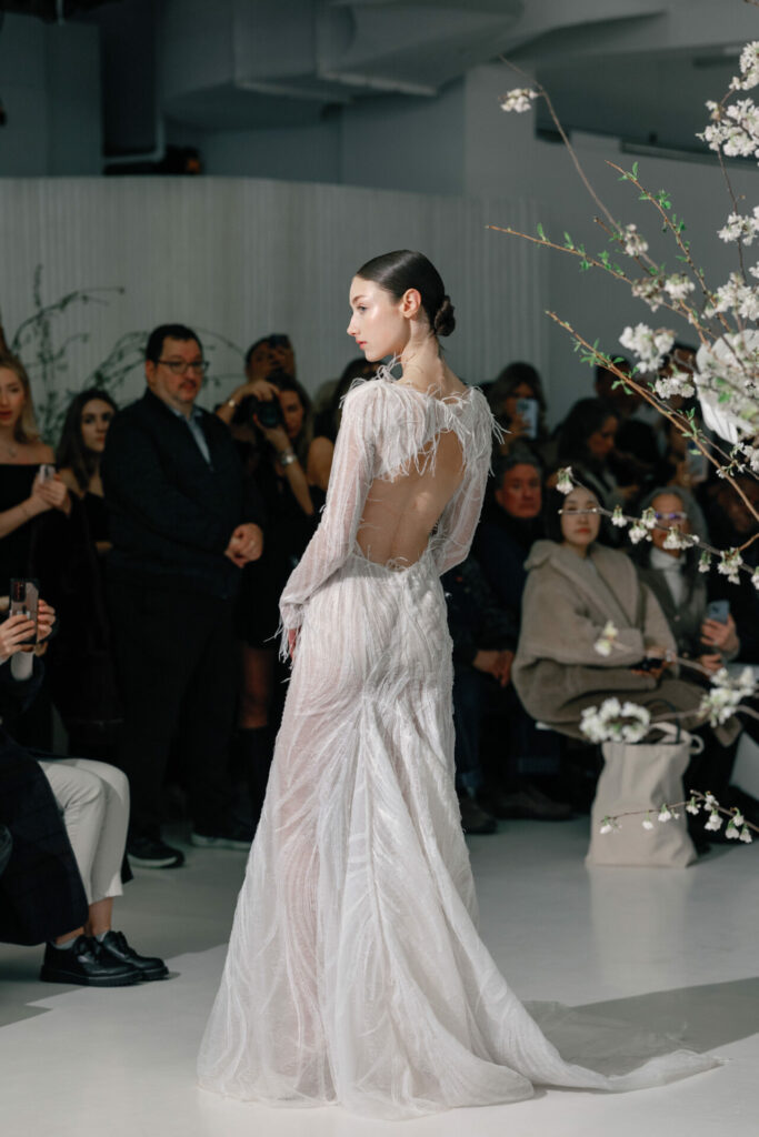 Model wearing the sheer Anouka wedding dress by Mira Zwillinger on a floral runway