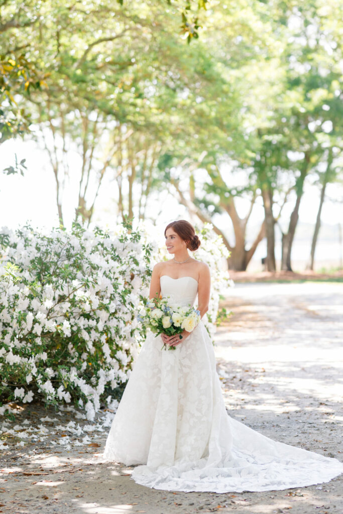 Bride in white gown holds bouquet outdoors.