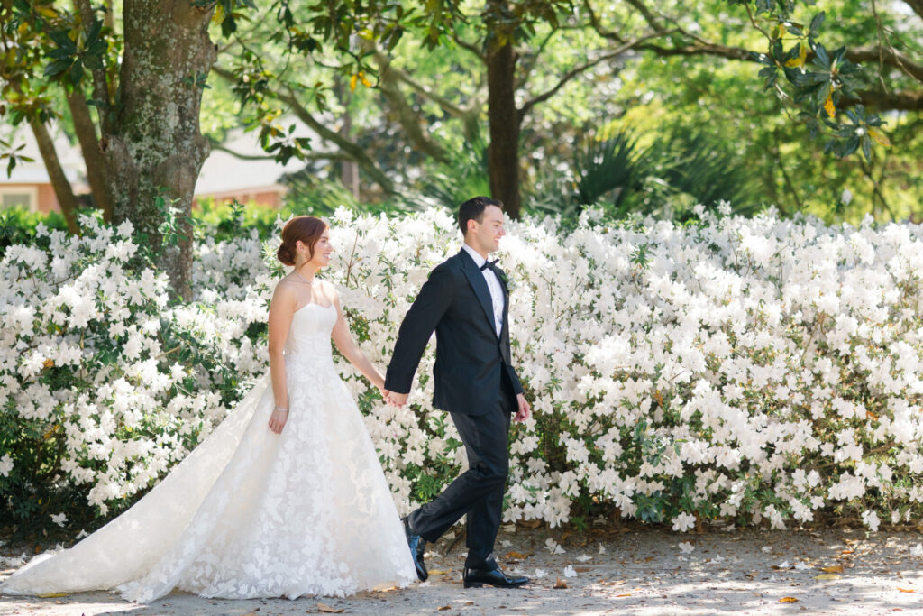 Bride and groom walk outdoors amid white blooms.