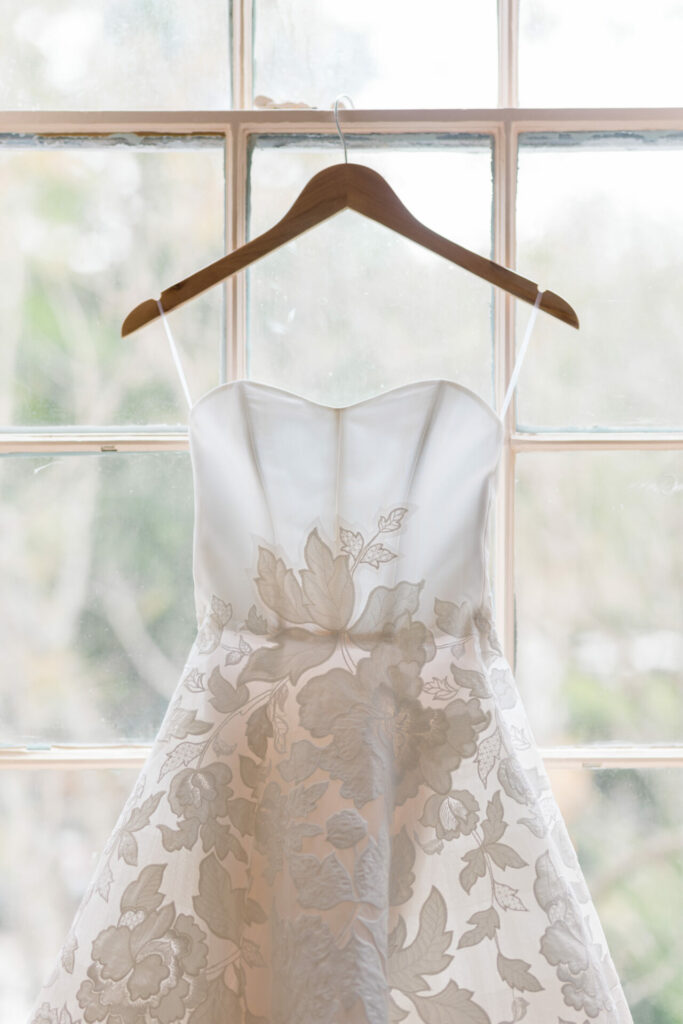 Luxury embroidered wedding gown on hanger by window.