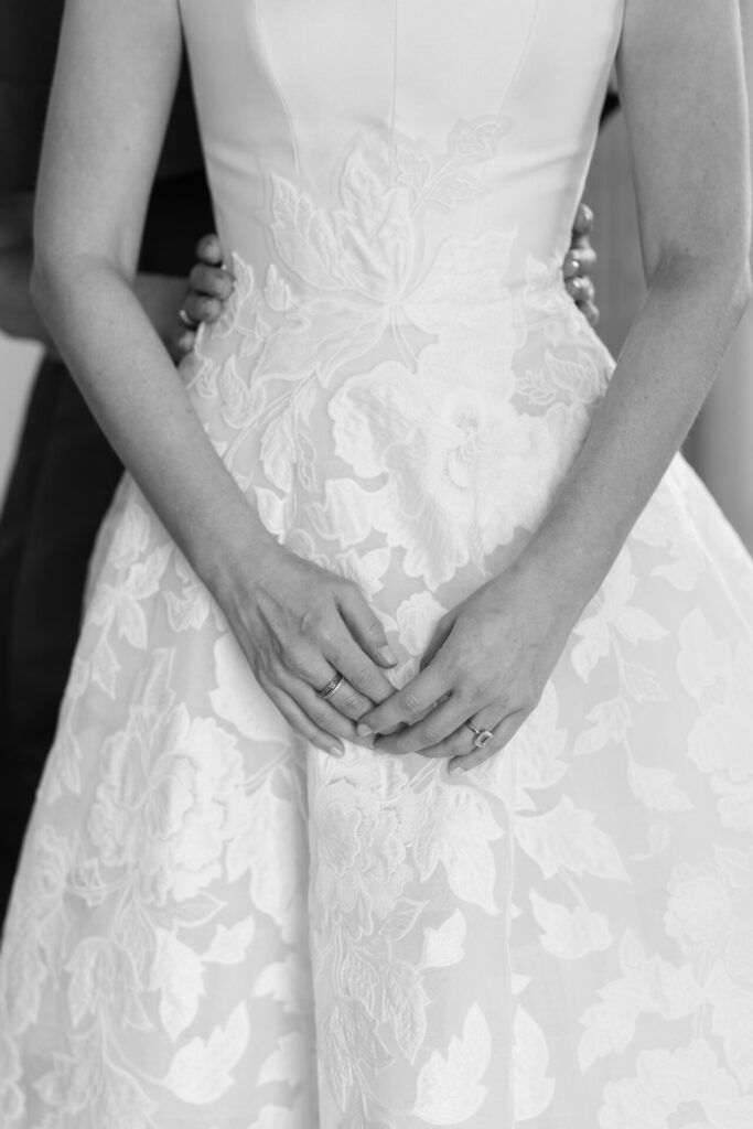 Bride in lace dress embraced from behind, monochrome.