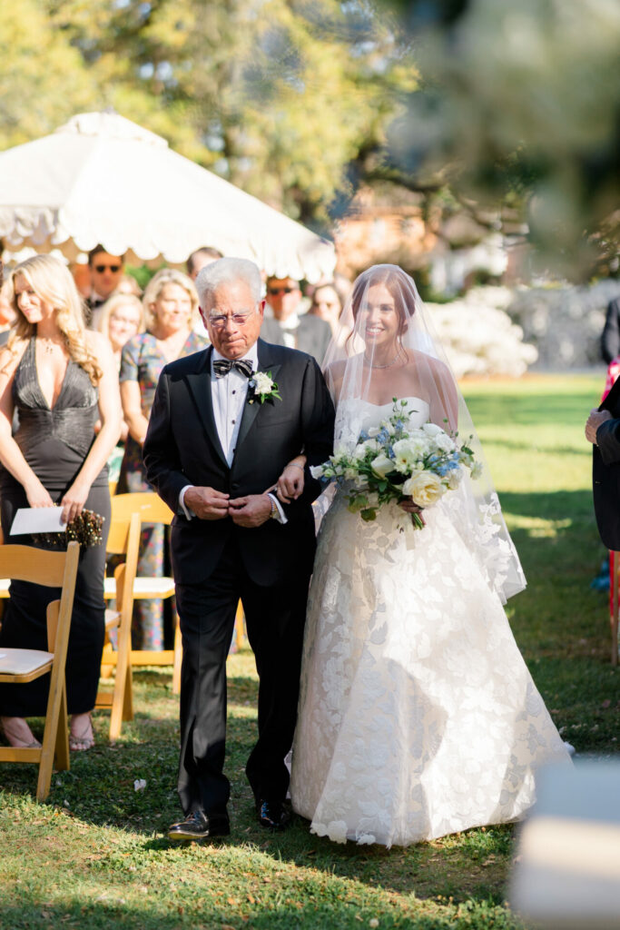 Bride in couture gown walks aisle with tuxedoed man.
