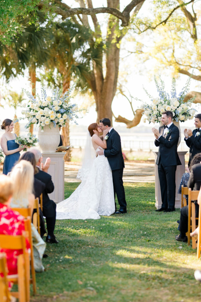 Bride and groom kiss amid luxury outdoor wedding.