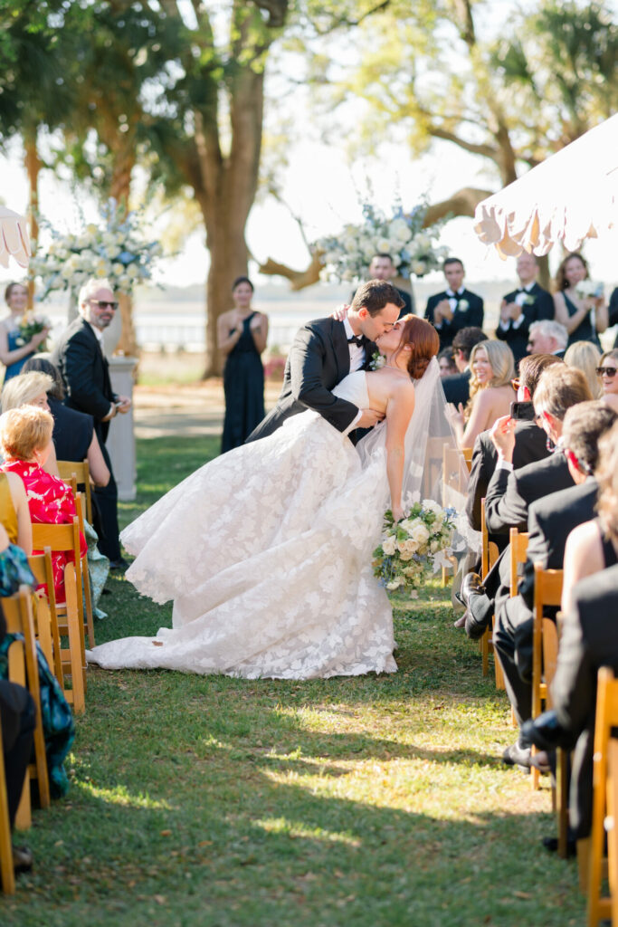 Bride and groom kiss amid elegant outdoor ceremony.