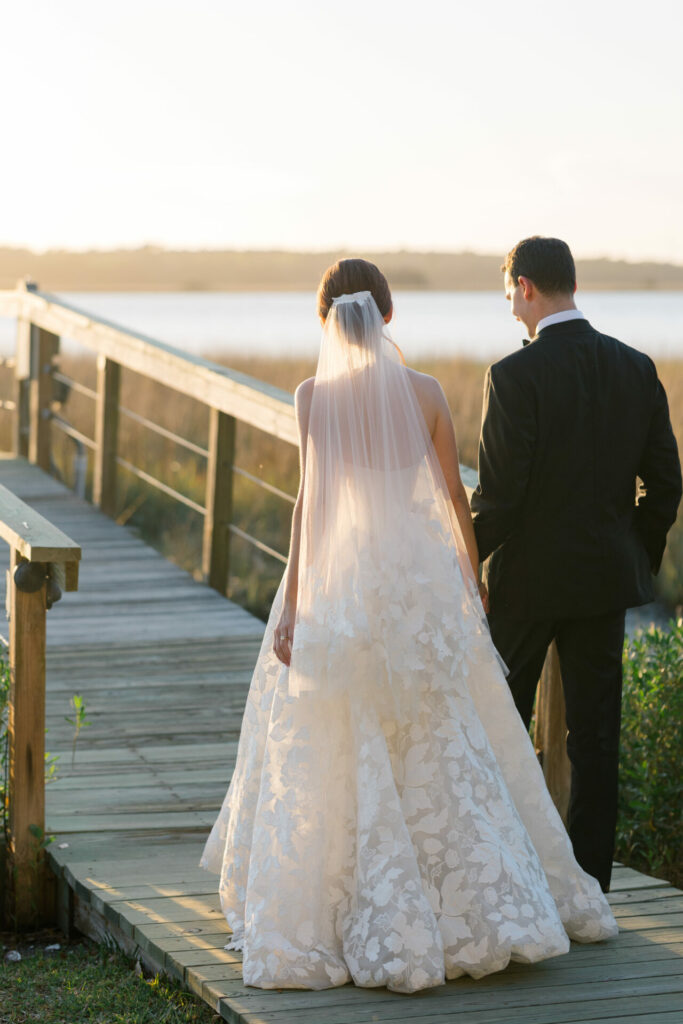 Bride and groom stroll boardwalk at sunset.