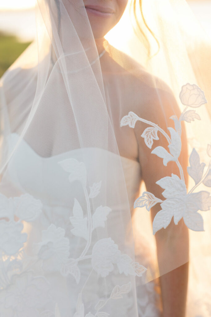 Bride’s lower face, shoulder, floral veil in sunlight.