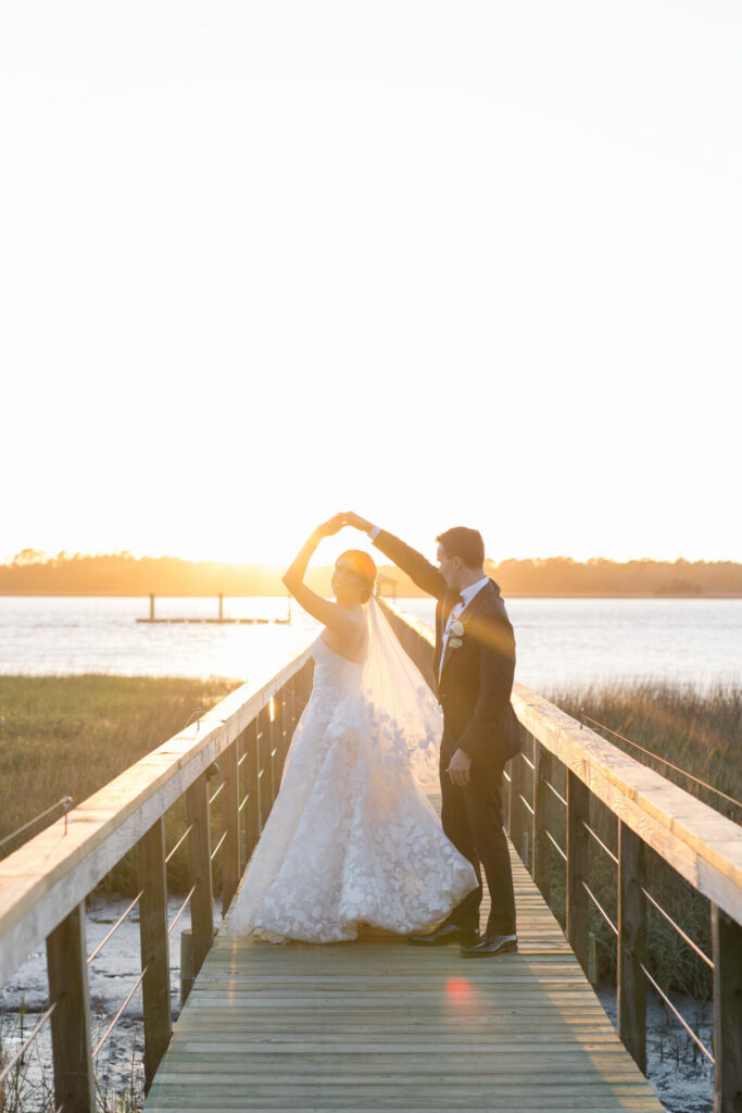 Bride and groom dance on dock at sunset.